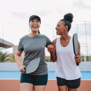 Two women holding pickleball paddles, smiling