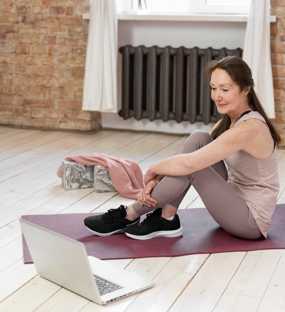 Woman exercising on yoga mat with laptop and cat nearby.