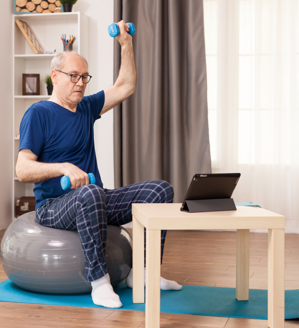 An elderly man exercising with dumbbells while sitting on a stability ball.