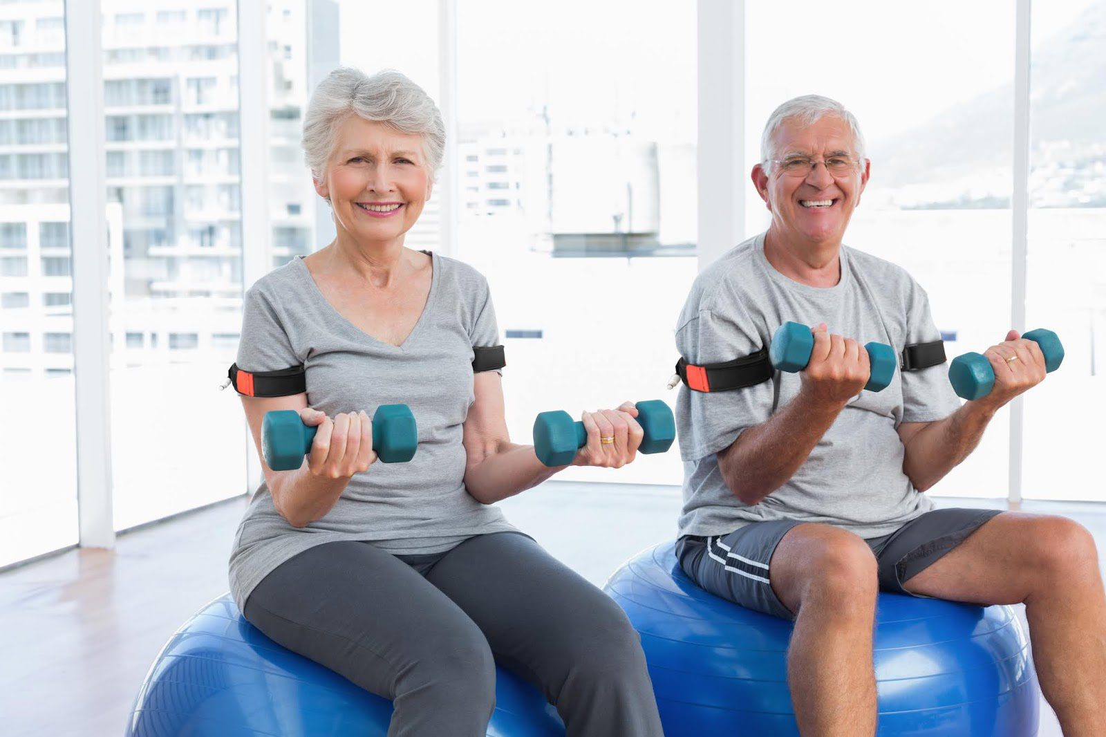 Senior couple exercising with dumbbells on stability balls indoors.