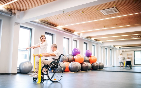 Therapist assisting a wheelchair user in a fitness studio with exercise.